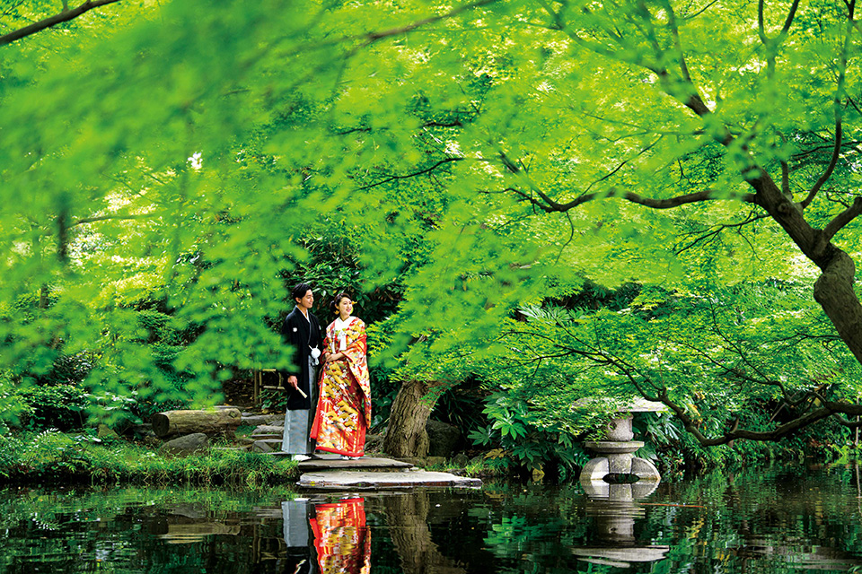 日本庭園の池のほとりに立つ和装の新郎新婦の様子
